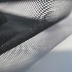 A close-up image features the 610mm Flyscreen Mesh by the Metre, unrolled on a white surface. The fine grid pattern of the black mesh is visible, with light casting gentle shadows that create a gradient effect on the surface below.