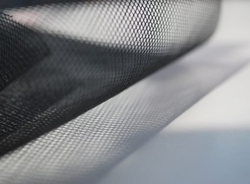 A close-up image features the 610mm Flyscreen Mesh by the Metre, unrolled on a white surface. The fine grid pattern of the black mesh is visible, with light casting gentle shadows that create a gradient effect on the surface below.