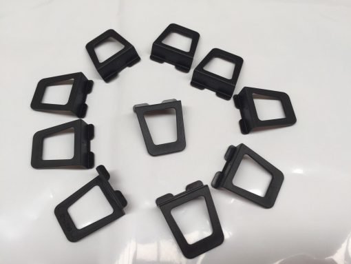 Ten black Finger Tabs are arranged in a circle on a white surface. Each tab features a rectangular opening and two protrusions on one end.